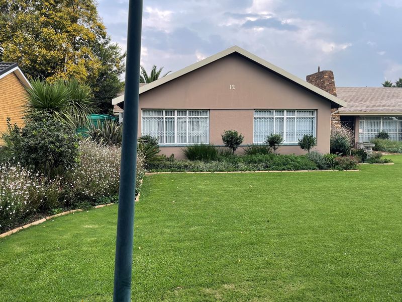 A well-maintained front exterior view of the house featuring a manicured lawn, established garden beds, and a classic gable roof design.