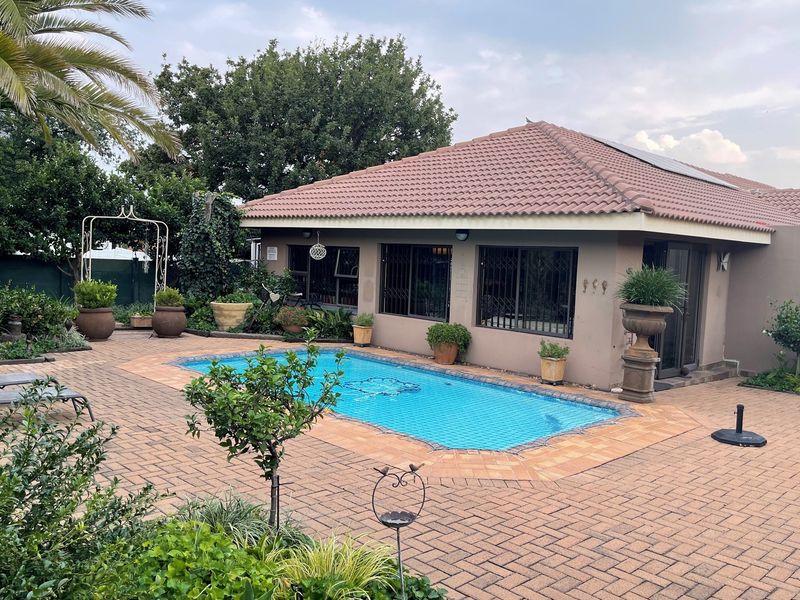 A well-maintained rear exterior view featuring a swimming pool, paved patio area, and established garden surrounding the house.