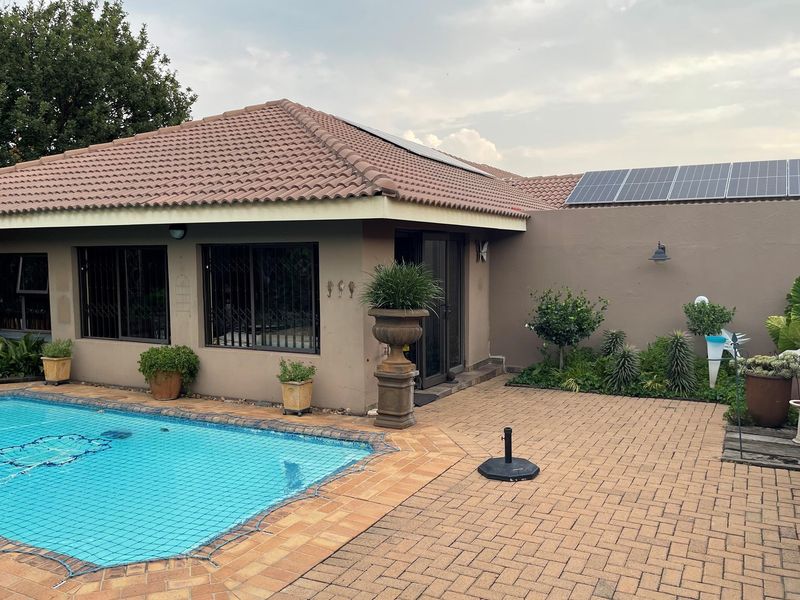 A well-maintained rear exterior featuring a swimming pool, paved patio area, and solar panels installed on the tiled roof.