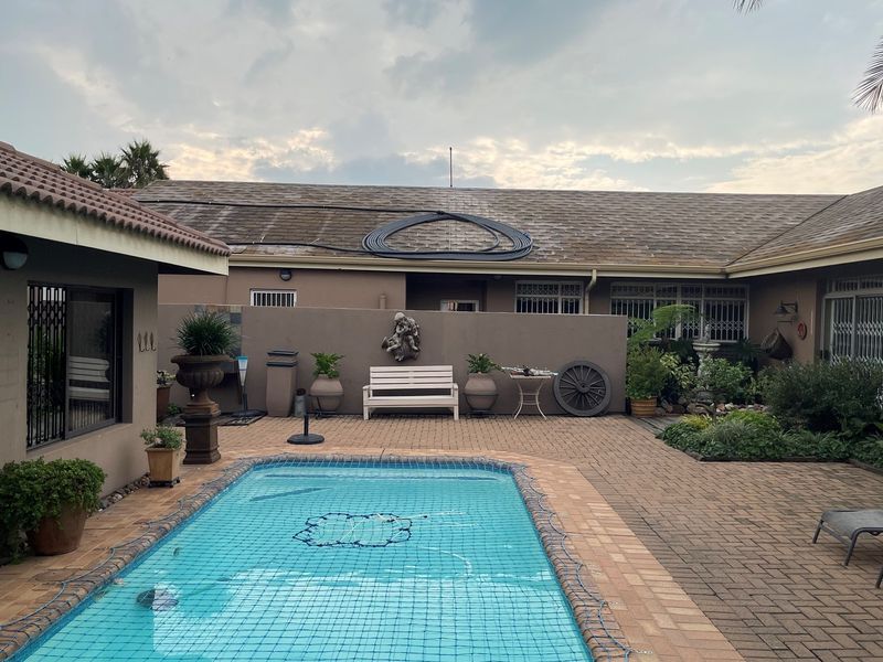 A rear courtyard featuring a swimming pool with a safety net, paved patio area, and exterior access to the main dwelling.