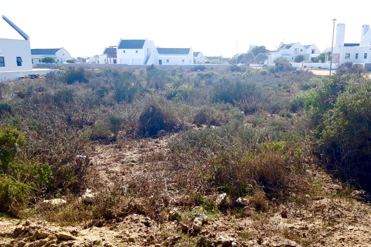 A vacant residential plot covered in natural coastal vegetation, situated within an established residential estate with surrounding homes.