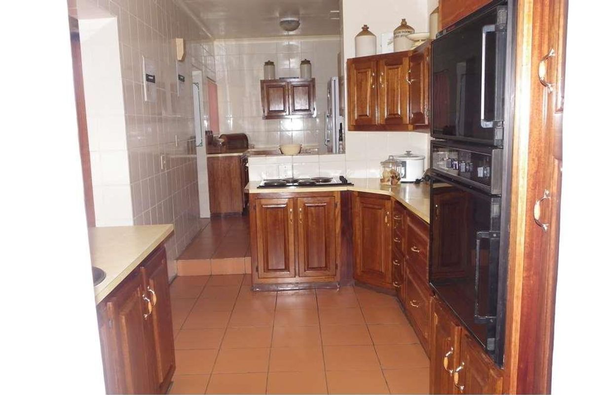 A dated kitchen featuring traditional wooden cabinetry, built-in oven, and tiled flooring, offering a functional layout with potential for modern renovation.