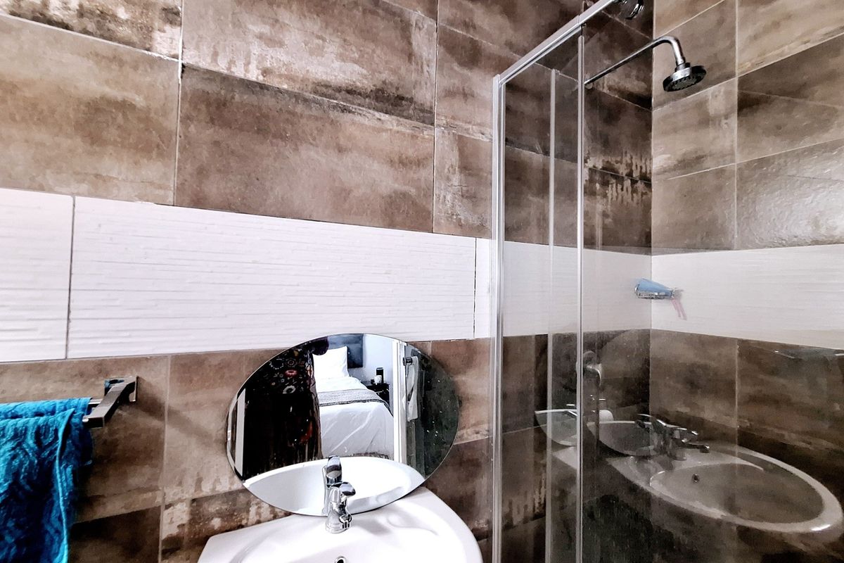 A modern bathroom featuring brown and white wall tiling, a glass-enclosed walk-in shower, and a pedestal basin with a mixer tap.