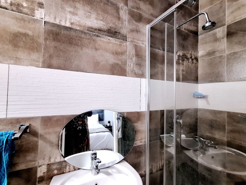 A modern bathroom featuring brown and white wall tiling, a glass-enclosed walk-in shower, and a pedestal basin with a mixer tap.