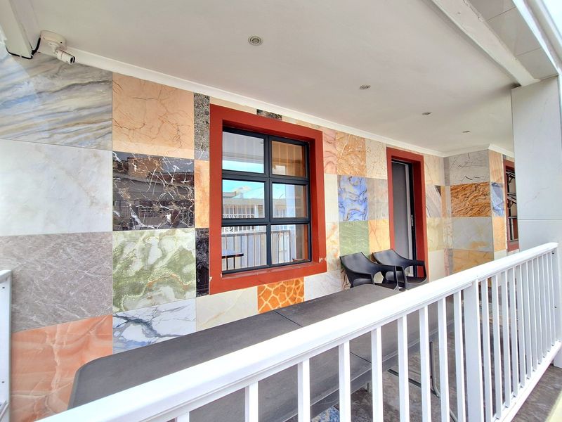 A covered patio area featuring decorative multi-patterned wall tiling, recessed ceiling lighting, and a white metal safety balustrade.