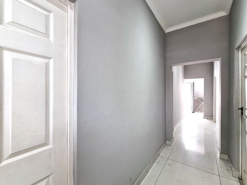 A clean, neutral-toned hallway featuring tiled flooring, white panel doors, and simple cornice detailing, providing a bright transition between living spaces.