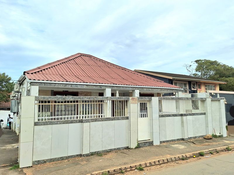Front elevation of a residential property featuring a tiled boundary wall, metal security fencing, and a corrugated metal roof.