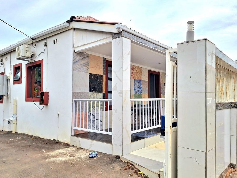 Front exterior view of the house featuring a covered patio with tiled finishes, metal balustrades, and a gated entrance.