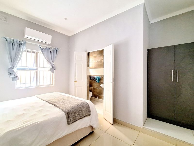 A well-maintained bedroom featuring tiled flooring, a built-in wardrobe, a split-system air conditioner, and direct access to an en-suite bathroom.