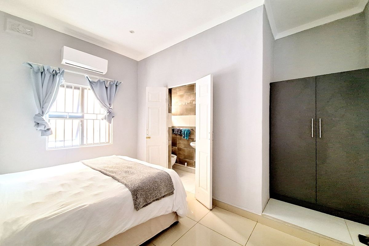A well-maintained bedroom featuring tiled flooring, a built-in wardrobe, a split-system air conditioner, and direct access to an en-suite bathroom.