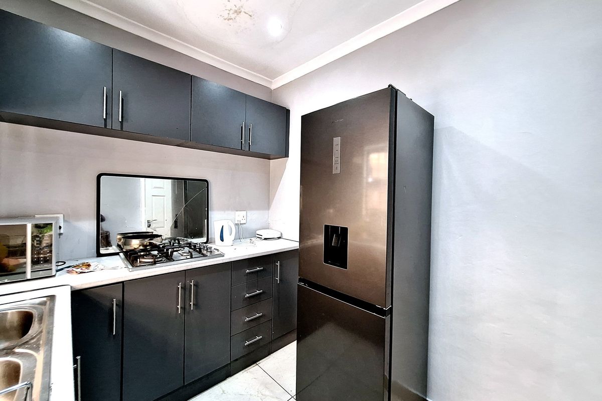 Compact kitchen featuring dark cabinetry, a gas hob, and tiled flooring. The space includes a built-in sink and overhead storage units.