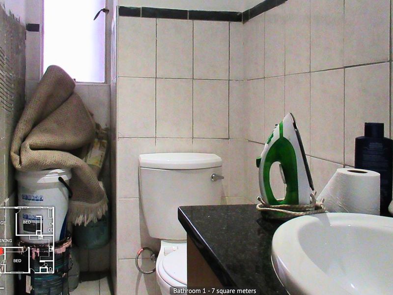 A compact bathroom featuring a standard toilet, vanity basin, and tiled walls. The space requires maintenance and cosmetic updates to improve its overall condition.