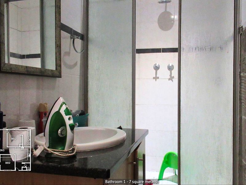 Bathroom featuring a vanity with granite countertop, drop-in sink, and a glass-enclosed shower area with visible wall tile damage.