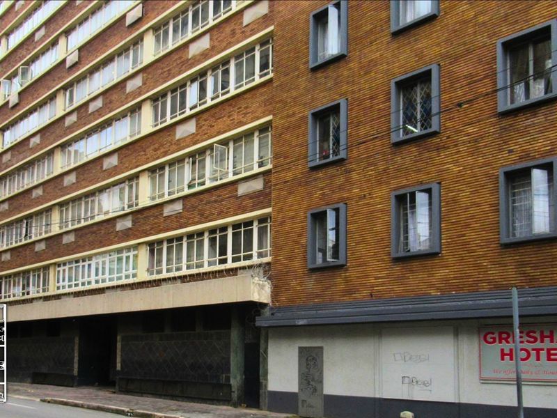 Exterior view of a multi-story brick apartment building featuring large windows and street-level signage.