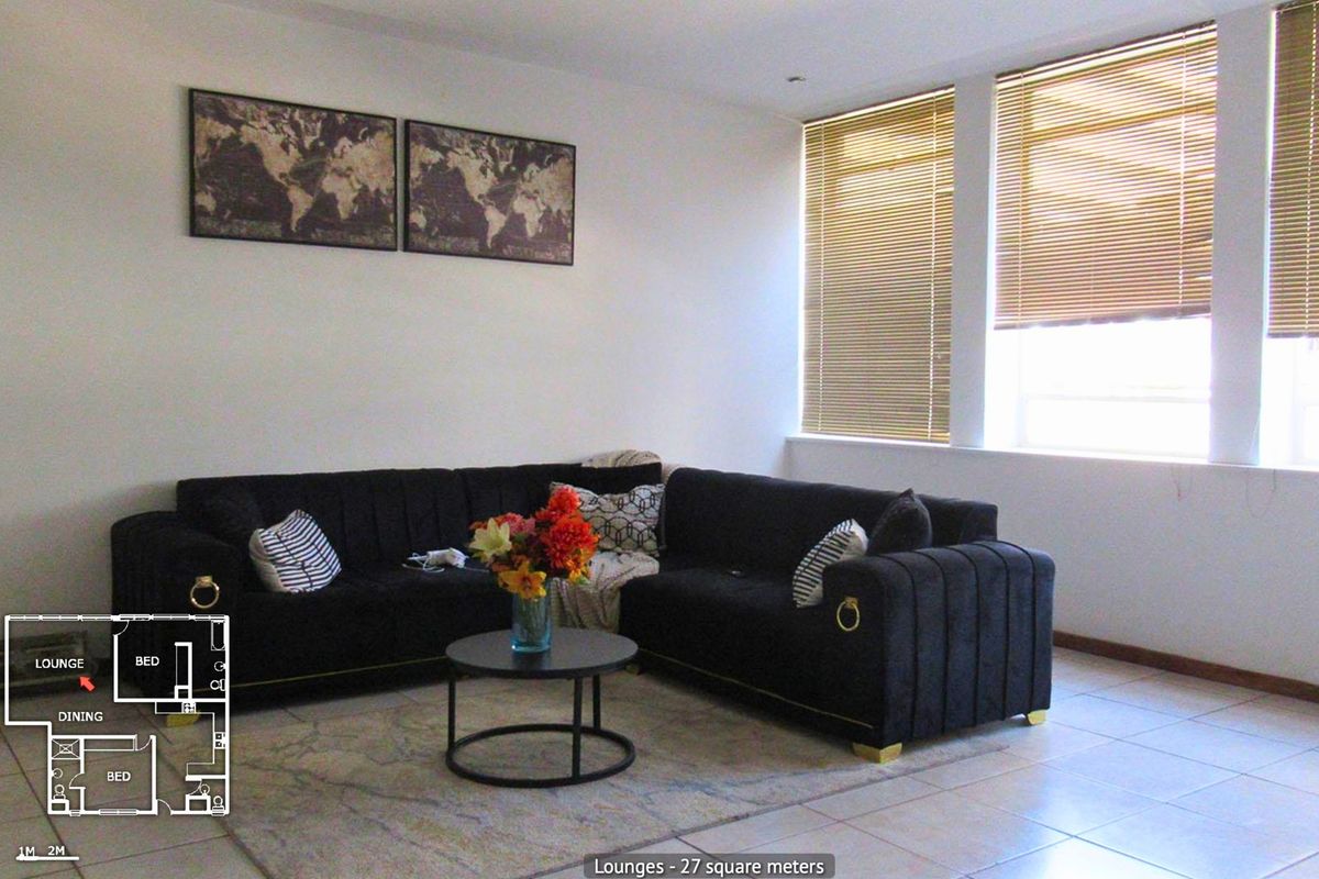A bright living room featuring tiled flooring, recessed downlighting, and large windows fitted with venetian blinds.