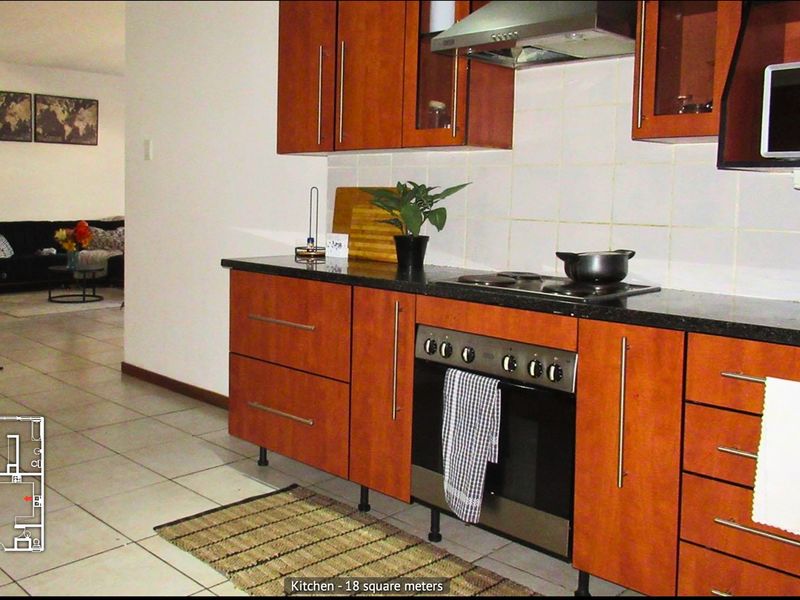 A functional kitchen featuring wood-finish cabinetry, granite countertops, and integrated appliances, with tiled flooring and a view into the adjacent living area.