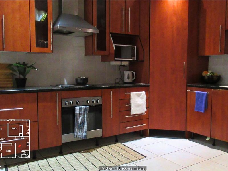 A functional kitchen featuring dark wood cabinetry, stone countertops, built-in oven, hob, and extractor fan with tiled flooring.