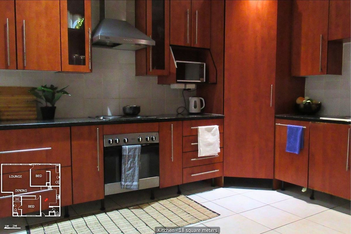 A functional kitchen featuring dark wood cabinetry, stone countertops, built-in oven, hob, and extractor fan with tiled flooring.