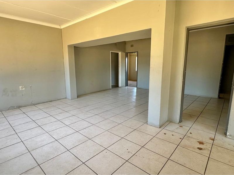 An empty, open-plan living area featuring neutral wall paint and ceramic floor tiles, providing a blank canvas for renovation and interior design.