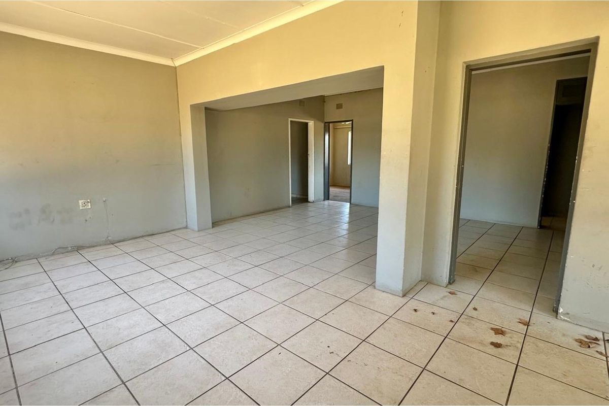 An empty, open-plan living area featuring neutral wall paint and ceramic floor tiles, providing a blank canvas for renovation and interior design.