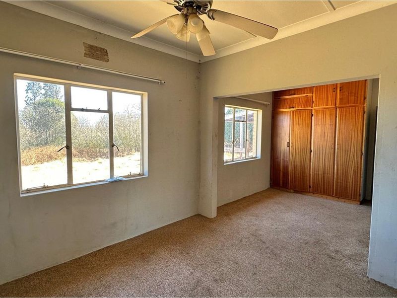 Spacious bedroom featuring built-in wooden cupboards, carpeted flooring, and a ceiling fan, offering a blank canvas for renovation and modernization.