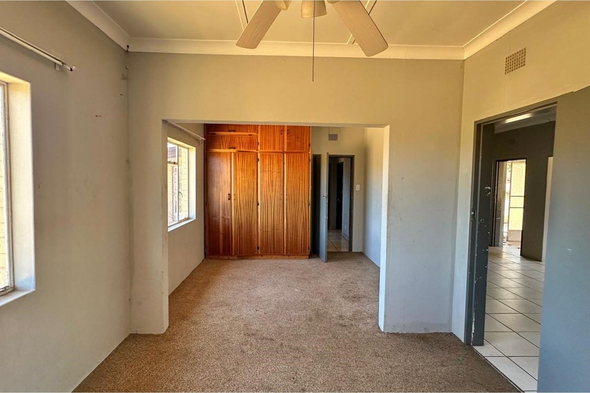 An empty bedroom featuring built-in wooden cupboards, a ceiling fan, and carpeted flooring, offering a blank canvas for renovation.