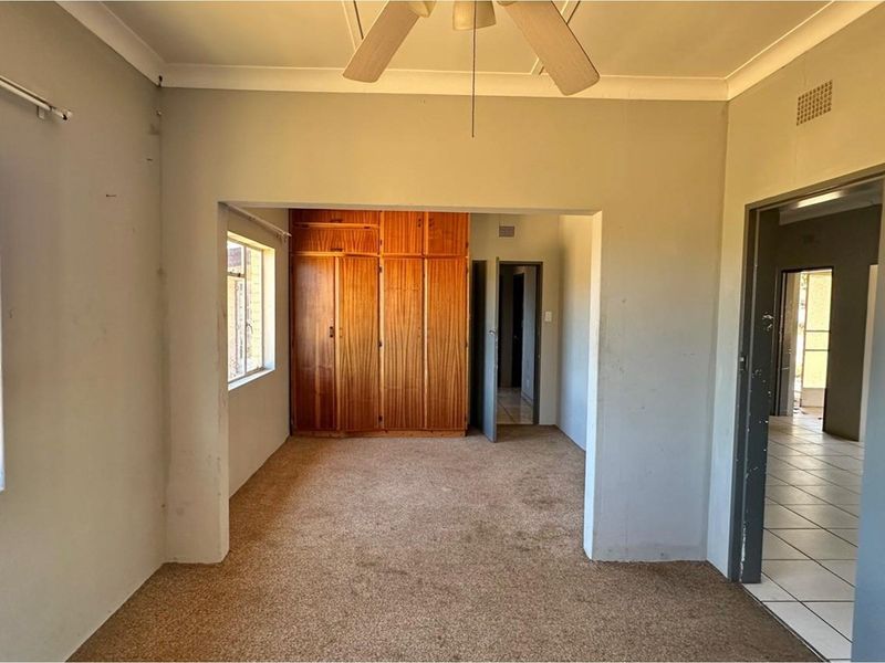 An empty bedroom featuring built-in wooden cupboards, a ceiling fan, and carpeted flooring, offering a blank canvas for renovation.