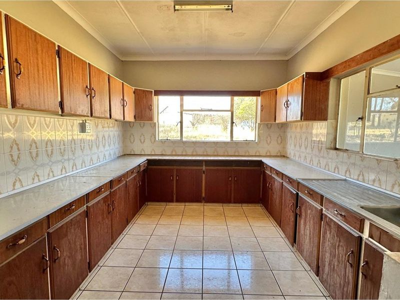 A spacious, empty kitchen featuring extensive wooden cabinetry, tiled flooring, and a tiled backsplash, offering a blank canvas for modern renovation.