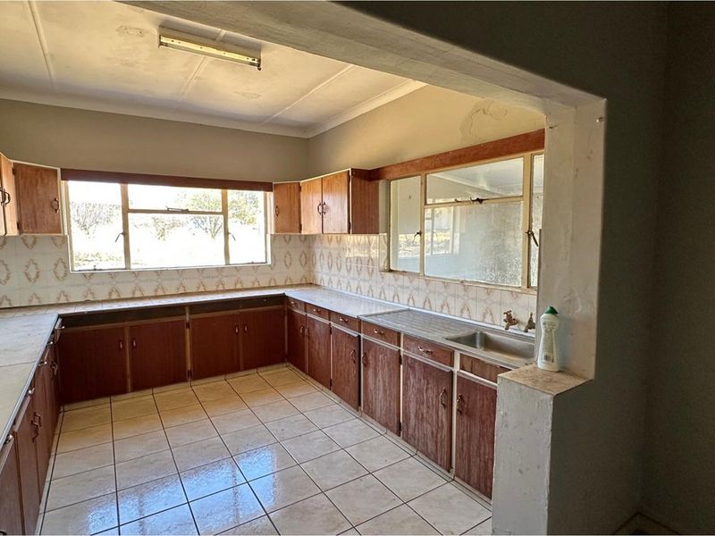A dated kitchen featuring original laminate cabinetry, tiled splashbacks, and tiled flooring, offering a blank canvas for a modern renovation.