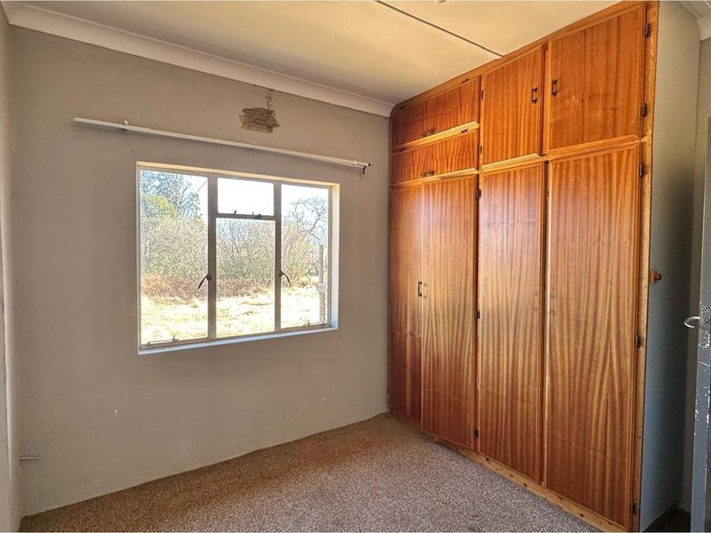 A vacant bedroom featuring built-in wooden cupboards, carpeted flooring, and a window with views of the exterior.