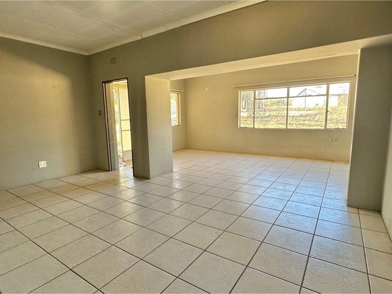 An empty, open-plan living area featuring neutral tiled flooring, large windows providing natural light, and a coved ceiling.