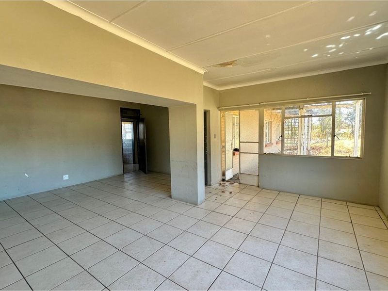An empty, open-plan living area featuring tiled flooring and large windows, requiring cosmetic updates and ceiling repairs.
