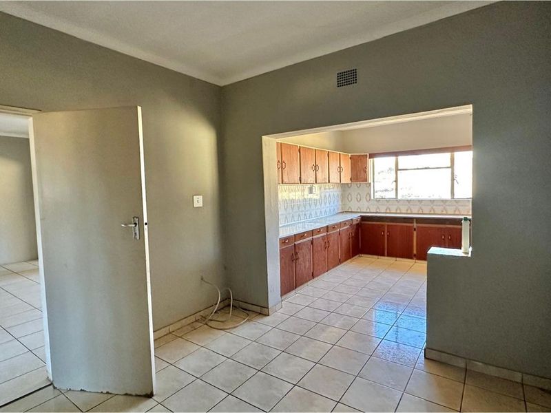 An open-plan kitchen area featuring tiled flooring and dated wooden cabinetry, offering a blank canvas for potential renovation and modernization.