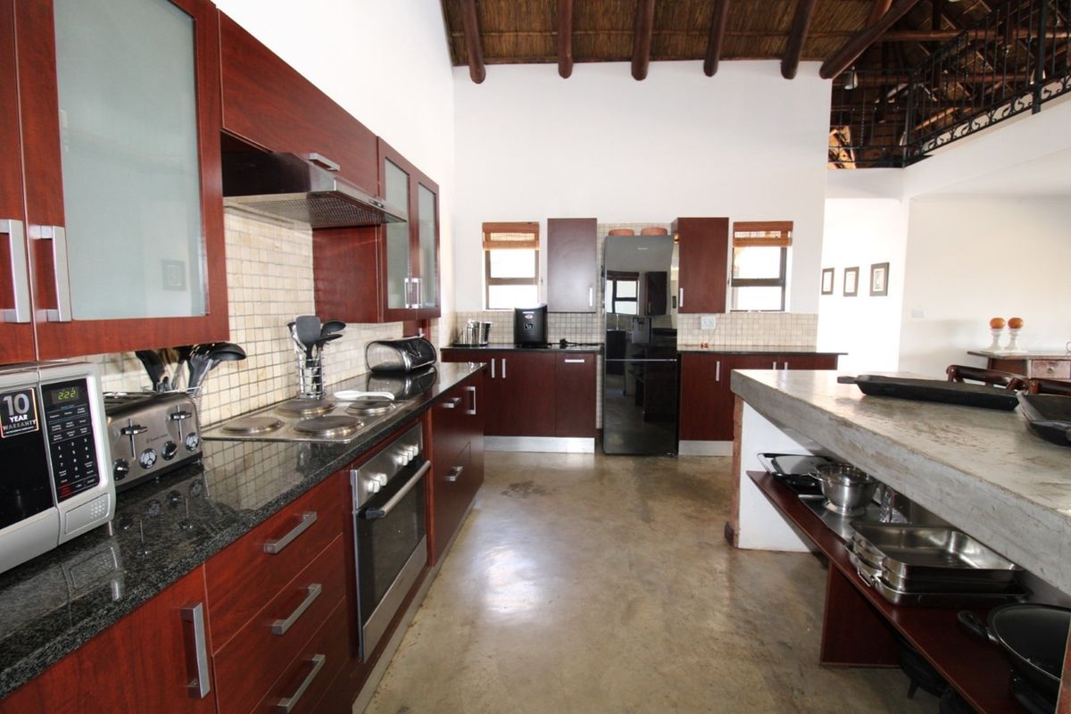 Spacious kitchen featuring dark wood cabinetry, granite countertops, a built-in oven and hob, and a unique concrete breakfast bar under a high thatched ceiling.