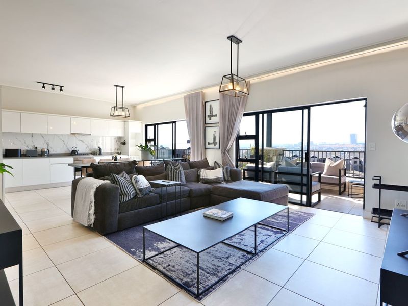 Modern open-plan living area featuring a sleek kitchen with marble-look backsplash, tiled floors, and large sliding doors leading to a balcony with city views.