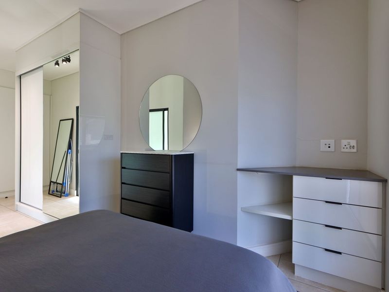 Modern bedroom featuring a built-in wardrobe with mirrored sliding doors, integrated vanity unit, and contemporary track lighting.