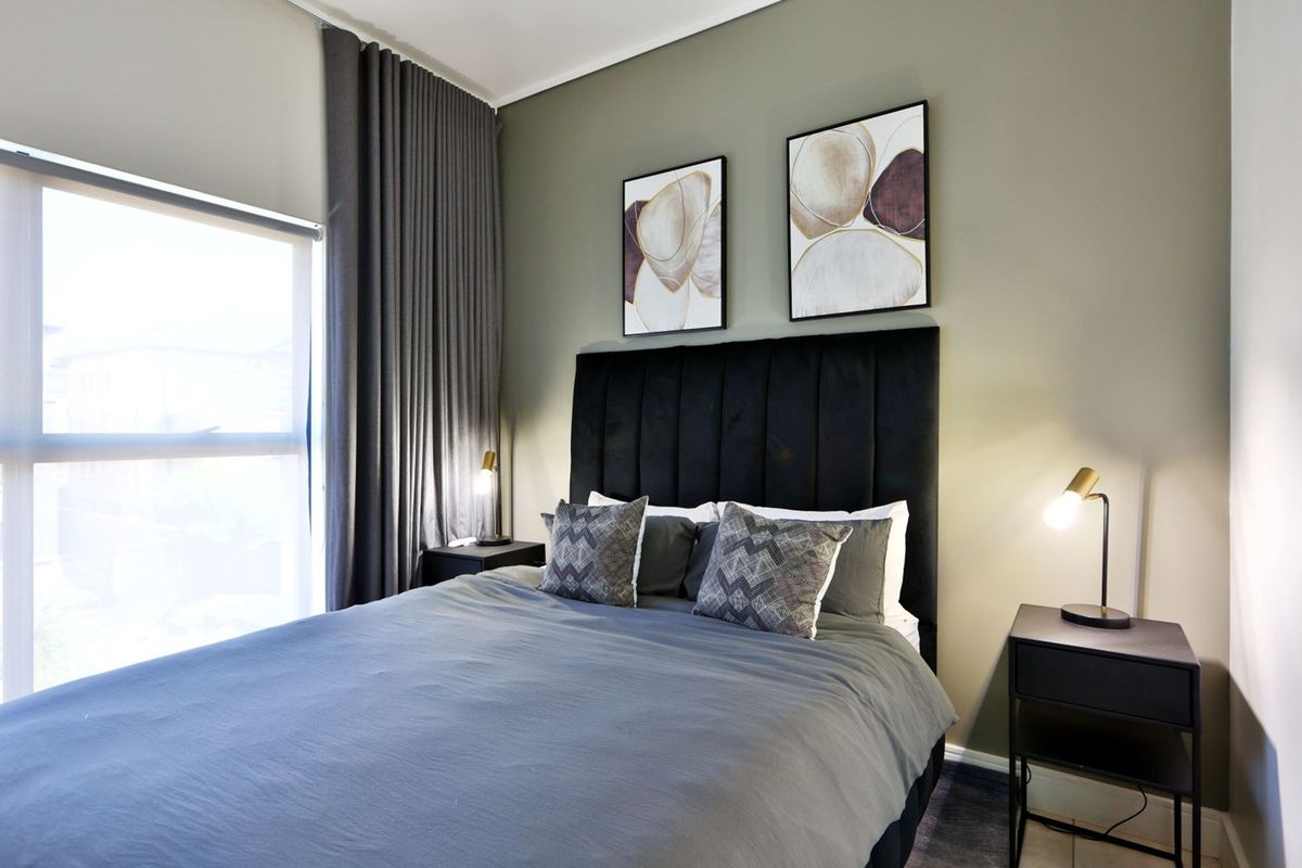 A well-lit bedroom featuring a large window with floor-to-ceiling curtains and a neutral wall finish.
