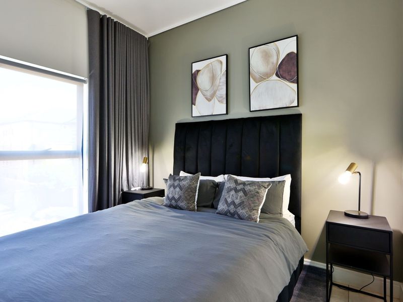 A well-lit bedroom featuring a large window with floor-to-ceiling curtains and a neutral wall finish.