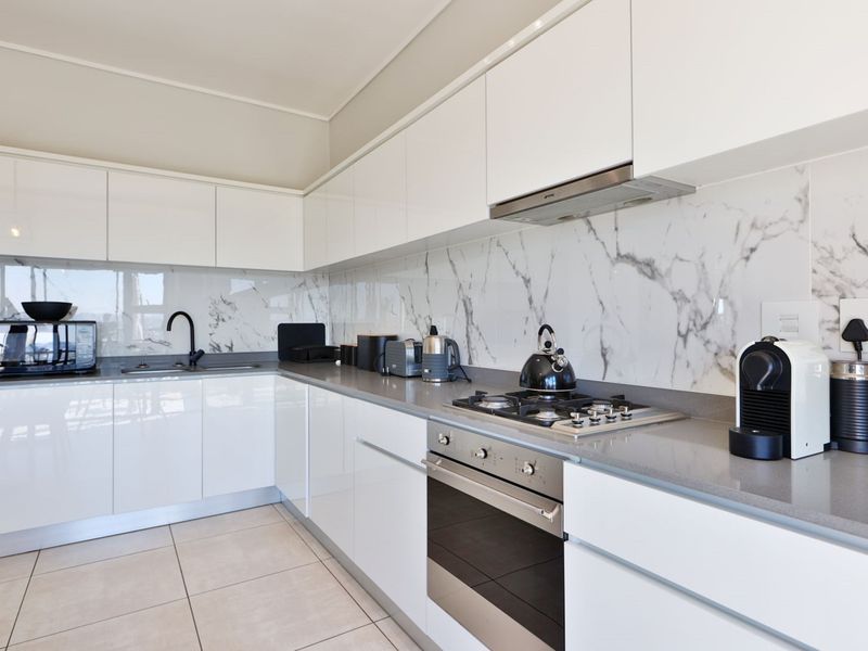 Modern kitchen featuring high-gloss white cabinetry, marble-look splashback, stone countertops, and integrated stainless steel appliances.