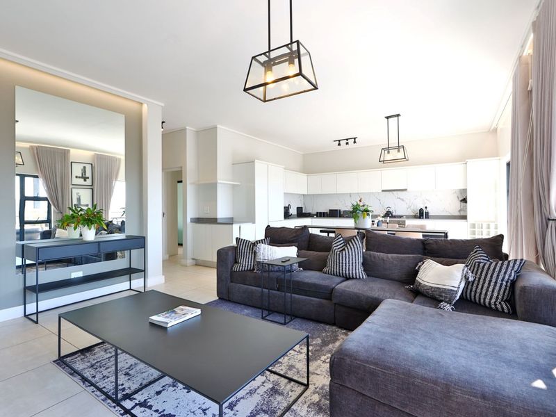 Modern open-plan living area featuring a sleek kitchen with marble-look backsplash, contemporary pendant lighting, and neutral tiled flooring throughout.