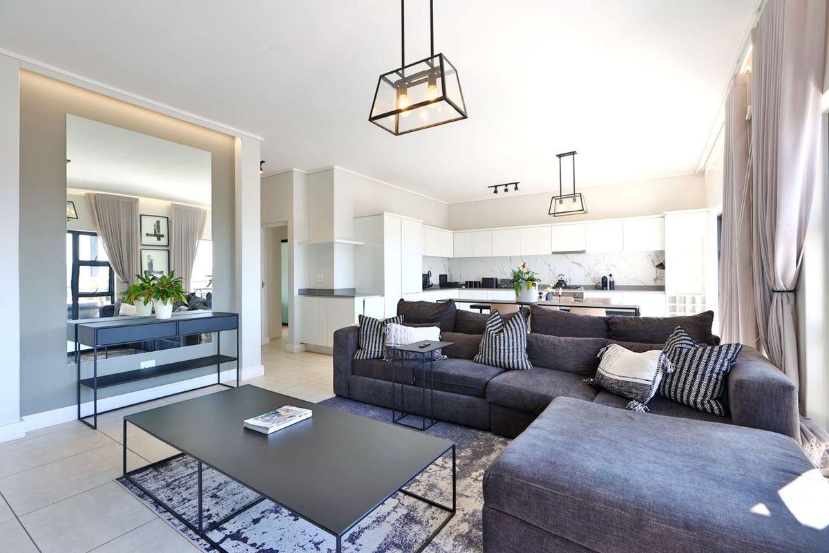 Modern open-plan living area featuring a sleek kitchen with marble-look backsplash, contemporary pendant lighting, and neutral tiled flooring throughout.