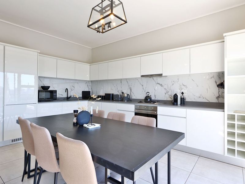 Modern open-plan kitchen featuring high-gloss white cabinetry, marble-look splashback, integrated appliances, and a dedicated wine rack, seamlessly flowing into the dining area.