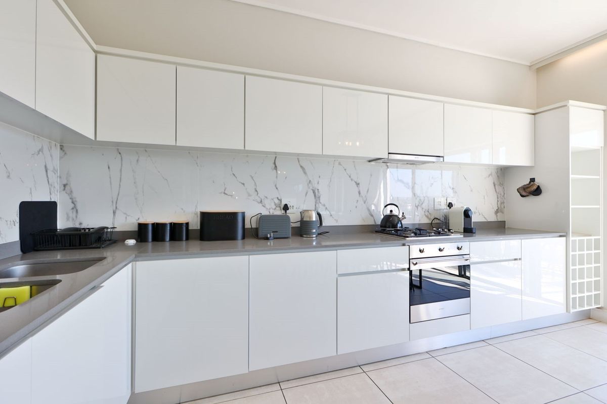 Modern kitchen featuring white gloss cabinetry, marble-look splashback, stone countertops, and integrated stainless steel appliances with tiled flooring.