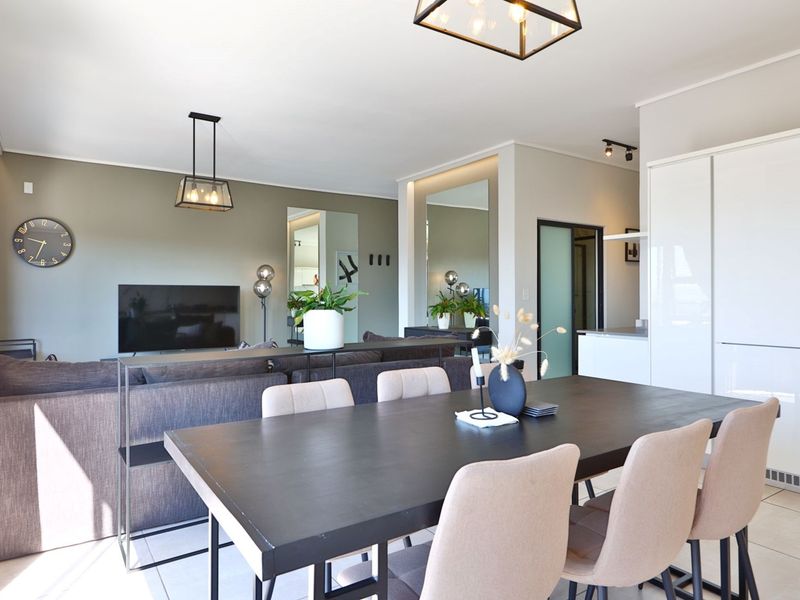 Modern open-plan living and dining area featuring sleek cabinetry, contemporary pendant lighting, and neutral tiled flooring in a well-maintained apartment setting.