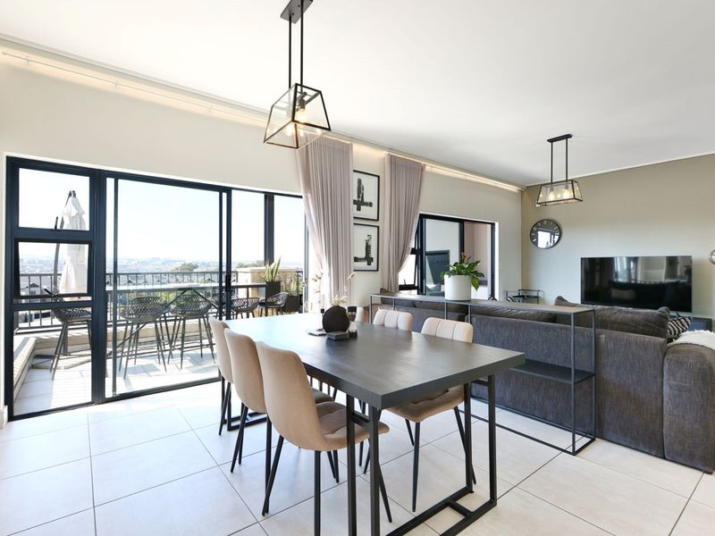 Modern open-plan living and dining area featuring large sliding glass doors leading to a balcony with expansive views and contemporary pendant lighting.
