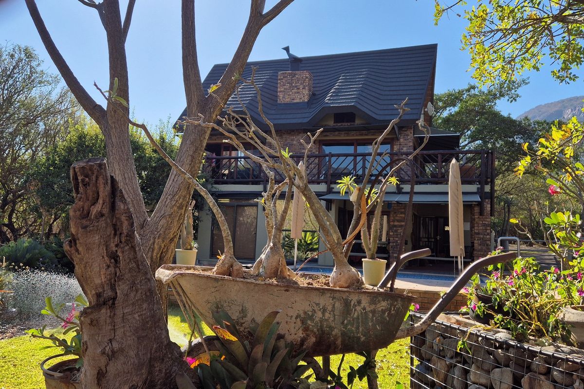 A view of the rear elevation of a multi-story brick house featuring a balcony, tiled roof, and chimney, set within a landscaped garden.