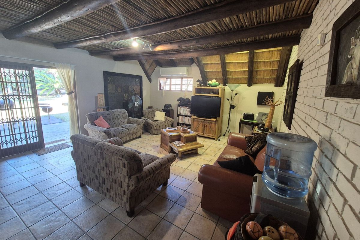 A rustic living room featuring a traditional thatched roof with exposed timber beams, tiled flooring, and sliding door access to the outdoor patio area.