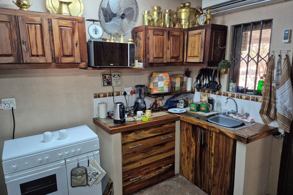 Compact kitchen featuring rustic wooden cabinetry, a built-in stove, stainless steel sink, and tiled backsplash with decorative accents.