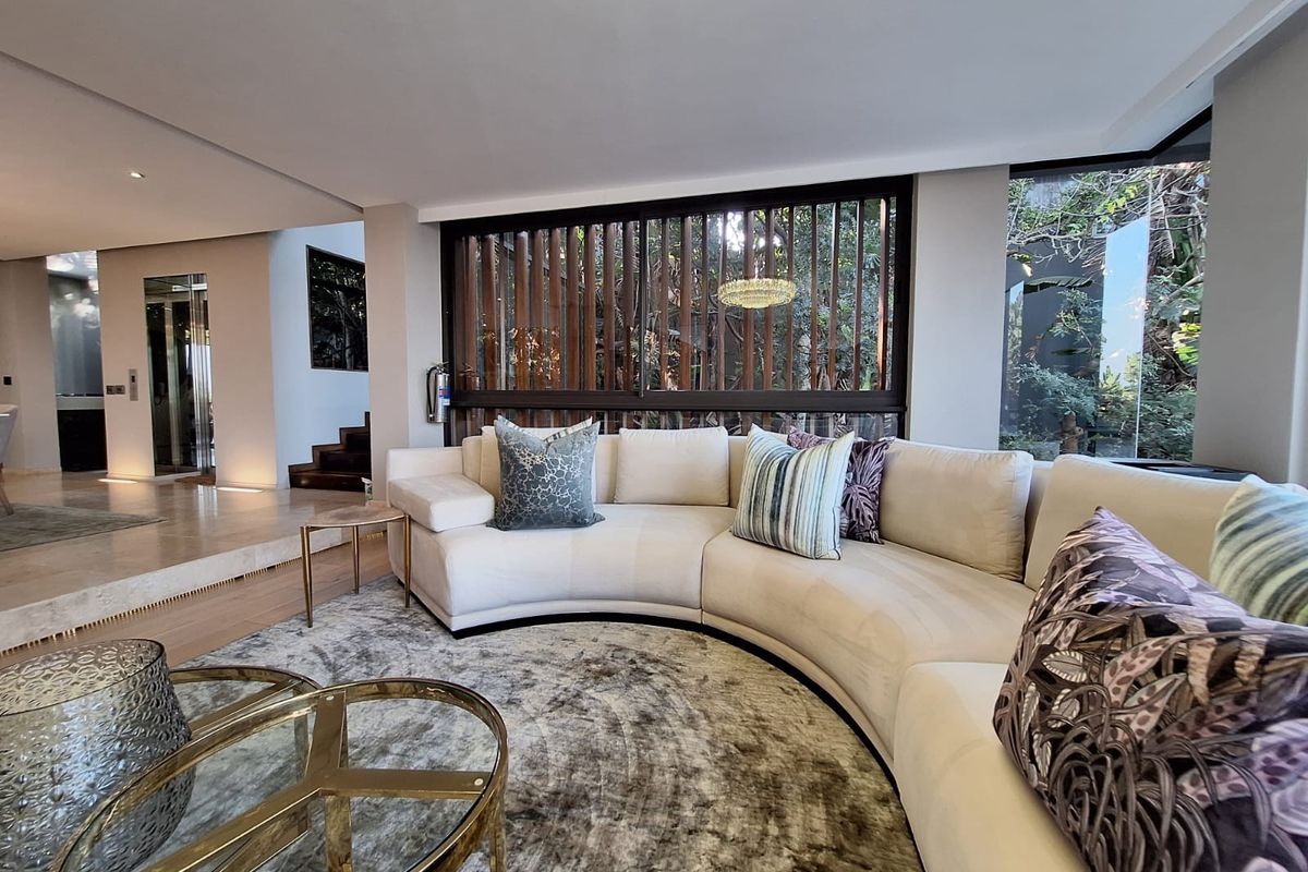 A sophisticated living room featuring high-end stone flooring, a unique timber slat window screen, and a modern glass elevator, creating a luxurious open-plan atmosphere.