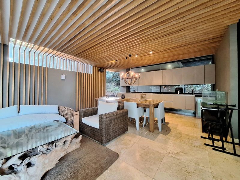 Modern open-plan living and kitchen area featuring a striking timber slat ceiling, stone flooring, and sleek built-in cabinetry.